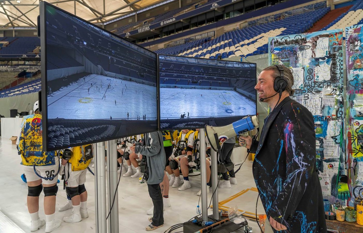 Der Künstler Christian Nienhaus dirigiert die Fussball-Spielerinnen und -Spieler, die am 5. Mai 2024 das Rekord-Kunstwerk - The Colourful Art of Football - in der Arena auf Schalke erstellt haben. (Bildrechte: Jochen Tack / TAS)